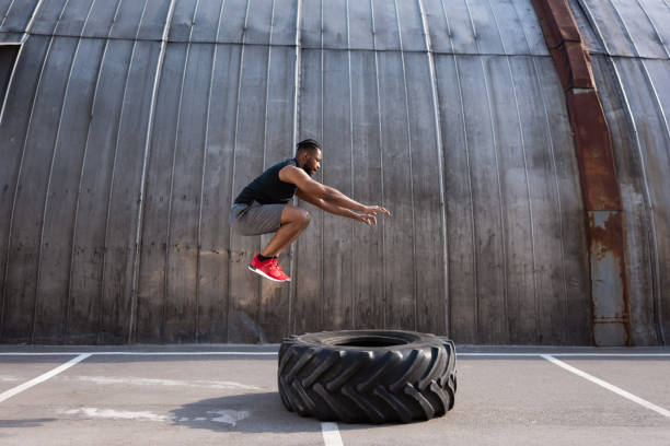 muskulösen afrikanischen amerikanischen sportler während des trainings mit reifen auf die straße springen - männliche figur stock-fotos und bilder