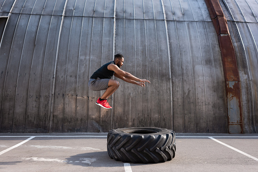 musculoso deportista afroamericano saltos durante el entrenamiento con el neumático en la calle photo