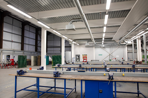 An empty engineering workshop can be seen with rows of workbenches in the room.