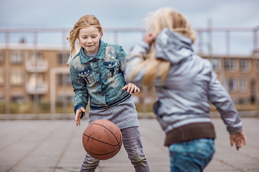 Blonde girl playing basketball on a streetball court