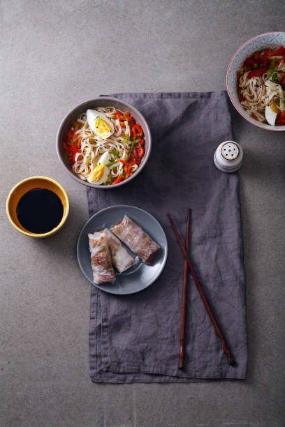 istock Lunch with udon noodles cooked with vegetables and spring rolls. Top view. Composition with copy space on concrete background 996232744