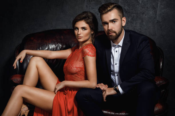 attraktives junges paar sitzt auf dem ledersofa - couple men fashion luxury stock-fotos und bilder