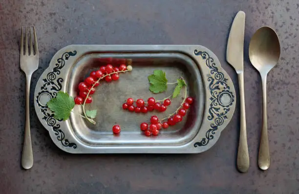 Redcurrants on a metal dish with fork and knife. Concept for healthy eating, dieting and antioxidant. Top view.