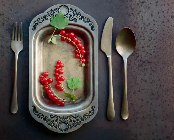 Redcurrants on a metal dish with fork and knife. Concept for healthy eating, dieting and antioxidant. Top view.