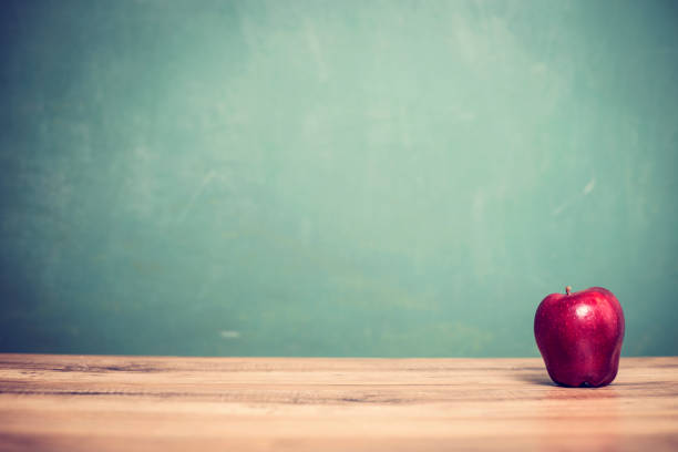 istock Red apple on wooden school desk with chalkboard. 996251220