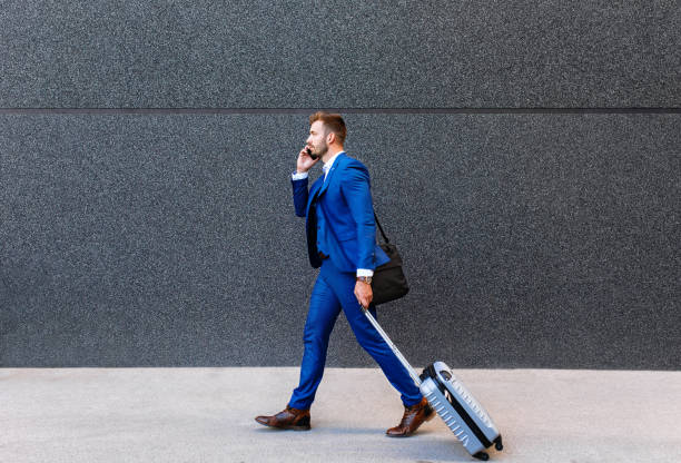 красивый молодой человек в командировке гуляет со своим багажом. - travel business business travel walking стоковые фото и изображения