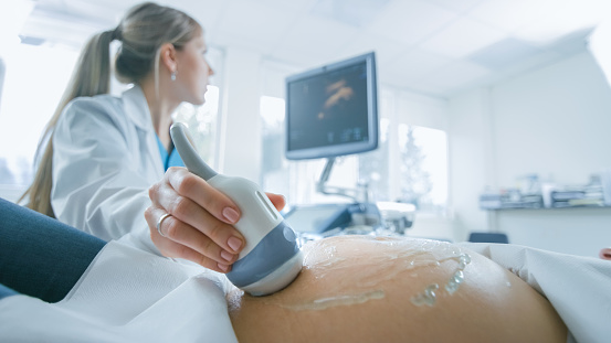 En el Hospital, toma de primer plano del Doctor hace ultrasonido / sonograma procedimiento a una mujer embarazada. Obstetra moviendo el transductor en el vientre de la madre del futuro. photo
