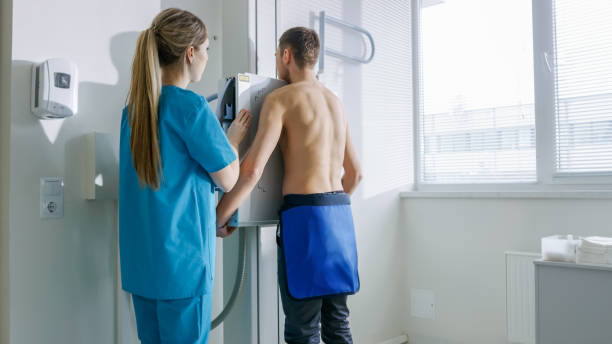 In the Hospital, Man Standing Face Against the Wall While Medical Technician Adjusts X-Ray Machine For Scanning. Scanning for Fractures, Broken Limbs, Chest, Cancer or Tumor. Modern Hospital with Technologically Advanced Medical Equipment. en el hospital, el hombre cara de pie contra la pared mientras que técnico médico ajusta la máquina de rayos x para escanear. análisis de las fracturas, roto de la extremidades, pecho, cáncer o tumor. moderno hospital con equipos médicos de tecnolog�