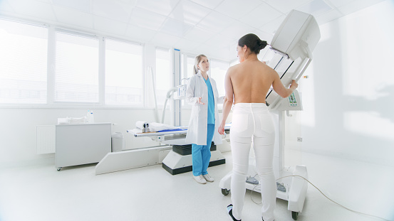 In the Hospital, Mammography Technologist / Doctor adjusts Mammogram Machine for a Female Patient. Friendly Doctor Explains Importance of Breast Cancer Prevention Screening. Modern Technologically Advanced Clinic with Professional Doctors.