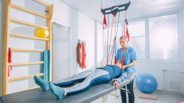 Physiotherapist Assists Female Patient with Trauma, Undergoing Rehabilitative Physiotherapy on a Special Suspension Rope System. Relieving Back Pain. Modern Clinic Using Most Advanced Rehabilitating Procedures. fisioterapeuta ayuda a paciente femenino con el trauma, sometidos a rehabilitación fisioterapia en un sistema de cuerda de suspensión especial. para aliviar el dolor de espalda. clínica moderna usando más avanzados procedimientos de rehabilitación.