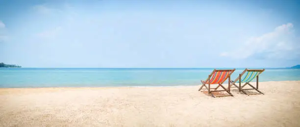 Two deckchairs on an idyllic deserted tropical beach facing out to sea