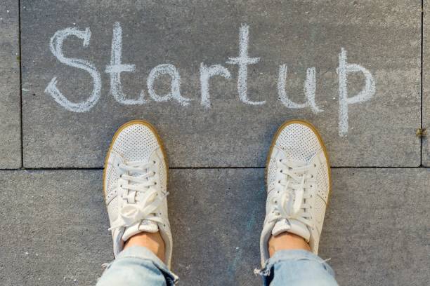 istock View from above, female feet with text startup written on grey sidewalk 996279470