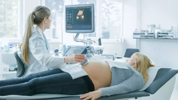 Photo of In the Hospital, Pregnant Woman Getting Ultrasound Screening, Obstetrician Checks Picture of the Healthy Baby on the Computer Screen. Happy Future Mother Waiting for her Baby to Born.