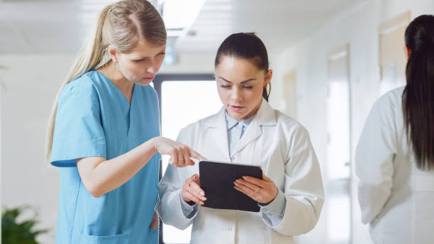 istock In the Hospital, Busy Doctors Talk, Using Tablet Computer While Standing in the Hallway. New Modern Fully Functional Medical Facility. 996286234