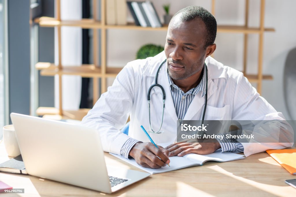 Concentrated foreigner preparing his scientific work Follow me. Attentive brunette looking at computer while sitting at workplace Doctor Stock Photo