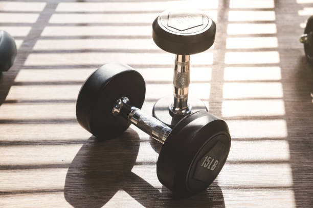 istock Dumbbell set indoor on brown wood floor with hard shadow from large window 996302314