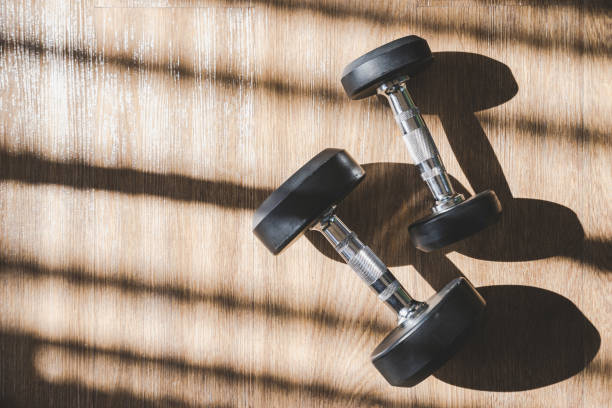 istock Dumbbell set indoor on brown wood floor with hard shadow from large window 996303592