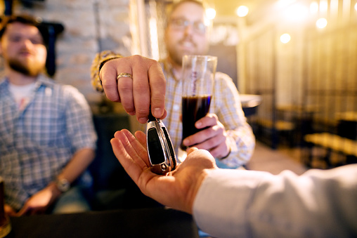 Drunk man with a beer in hand giving car key to the sober friend while enjoying in the bar. Close up focus view of key and hands.
