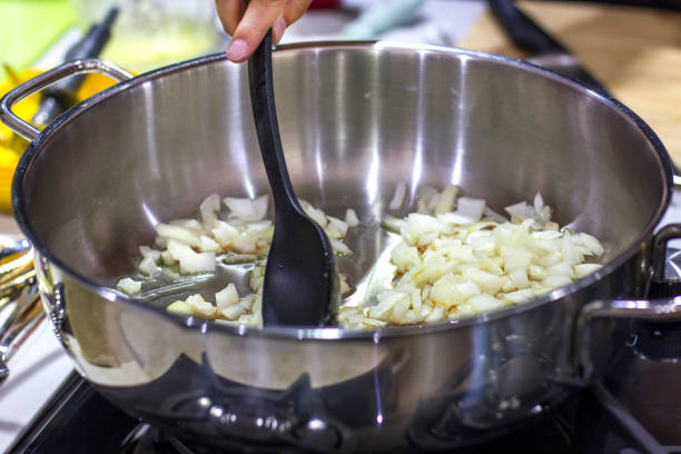 friggere a mano le cipolle in una grande casseruola, mescolandola con cucchiaio nero - 2546 foto e immagini stock