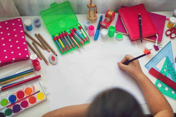 portrait of a beautiful young kid girl drawing on a white paper with color pencil at home