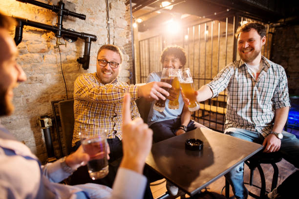Cheerful male friends clinking with draft beer in front of their friend with a glass of water in hand and rejecting alcohol. Cheerful male friends clinking with draft beer in front of their friend with a glass of water in hand and rejecting alcohol. sobriety stock pictures, royalty-free photos & images