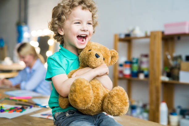 Cute Little Kid Hugging Teddy Bear Warm toned portrait of happy curly haired kid laughing cheerfully and hugging teddy bear toy, copy space stuffed toy stock pictures, royalty-free photos & images