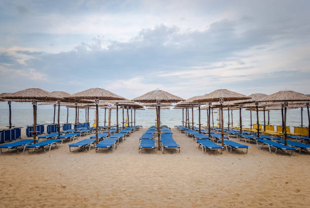 Empty deckchairs on the beach under parasols, overlooking the crystal blue sea. Empty deckchairs on the beach under parasols, overlooking the crystal blue sea. paralia stock pictures, royalty-free photos & images