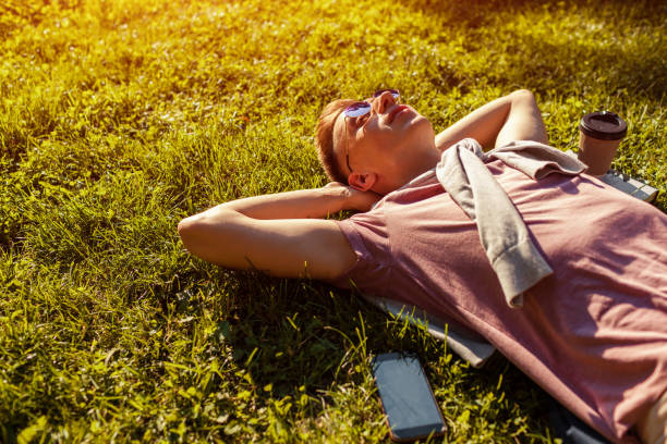 istock Handsome college man chilling in spring campus park. Happy guy student lying on grass with his phone and coffee beside 996371624