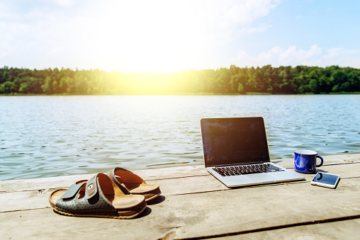 laptop with cup and phone one wooden dock. river on background. summer time. work with you