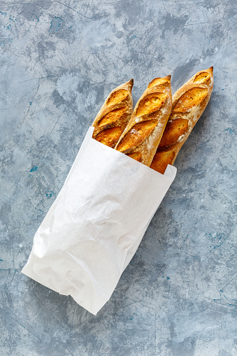 Paper bag with freshly baked artisanal baguettes on a gray concrete background. Top view.