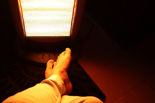 A Caucasian man's legs in front of an electric heater. Keeping warm in winter concept image.