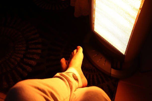 A Caucasian man's legs in front of an electric heater. Keeping warm in winter concept image. A Caucasian man's legs in front of an electric heater. Keeping warm in winter concept image. space heater stock pictures, royalty-free photos & images