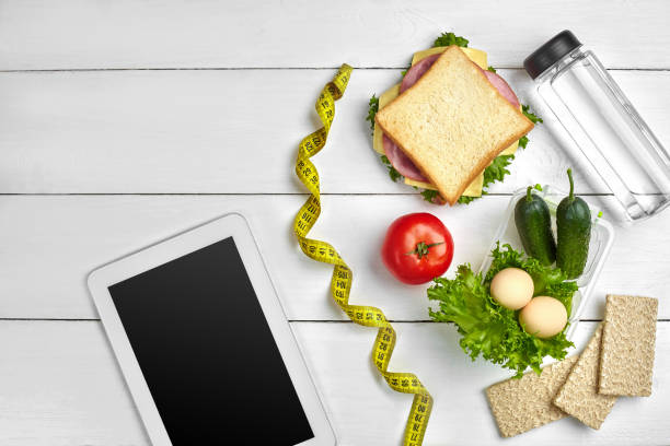 istock Sandwich, fresh vegetables, bottle of water and eggs on a table with a tablet, top view. Copy space 996413390