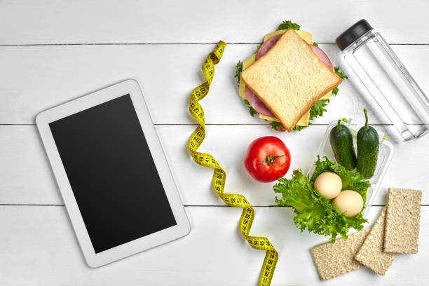 istock Sandwich, fresh vegetables, bottle of water and eggs on a table with a tablet, top view. Copy space 996415692