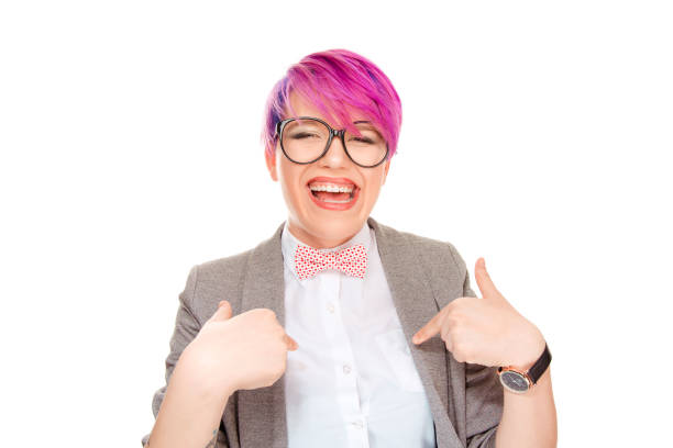 Cheerful millennial woman with pink hair wearing bow tie and glasses and pointing at herself cheerfully isolated on whit background. Confident pointig to herself