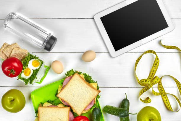 istock Sandwich, fresh vegetables, bottle of water and eggs on a table with a tablet, top view. Copy space 996435432