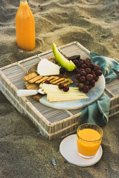 istock Seaside beach picnic on sand concept, bamboo table with cheese platter, 996437922