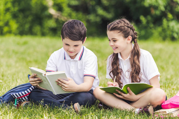 istock adorable schoolchildren doing homework together while sitting on grass in park 996448520