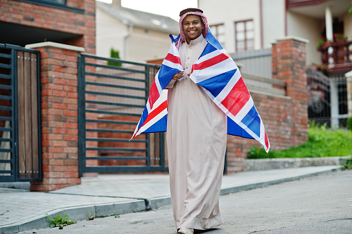 Middle Eastern arab man posed on street with Great Britain flag. England and Arabian countries concept.