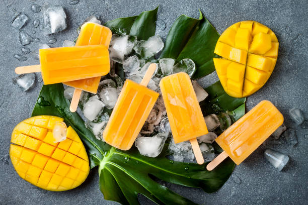 istock Mango popsicles over green tropical palm leaf on grey stone background. Overhead, top view 996472744