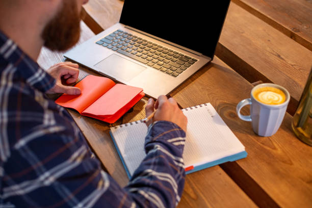 istock Cropped image of casual business man or freelancer planning his work on notebook, working on laptop computer with smart phone, cup of coffee on table at coffee shop or home office 996473576