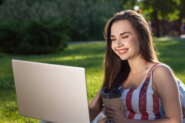 bela jovem sentada no laptop de uso de saco de feijão, enquanto descansava na grama no parque do sol - coffee bean bag human hand - fotografias e filmes do acervo