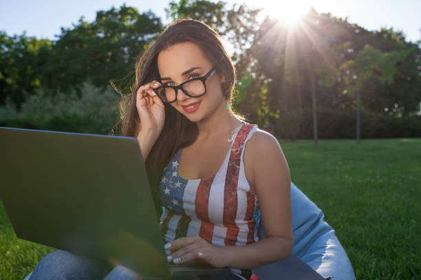 bela jovem sentada no laptop de uso de saco de feijão, enquanto descansava na grama no parque do sol - coffee bean bag human hand - fotografias e filmes do acervo