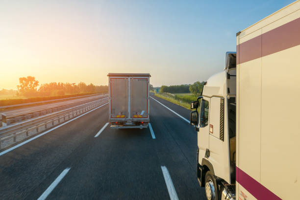 Two trucks driving motorway in early morning, sun flare effect stock photo
