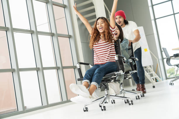 istock Group of multiethnic young creative teamwork having fun laughing and smiling in office chairs pushing. Coworker celebrating for success feeling happy, enjoy and excited in modern office workplace. 996508230