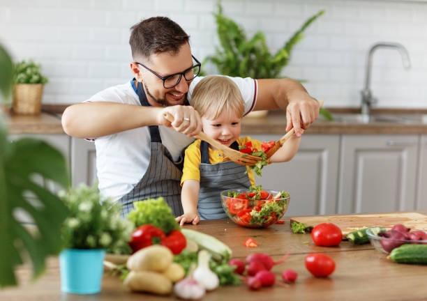 szczęśliwy ojciec rodziny z synem przygotowuje sałatkę warzywną - family with one child domestic life caucasian love zdjęcia i obrazy z banku zdjęć