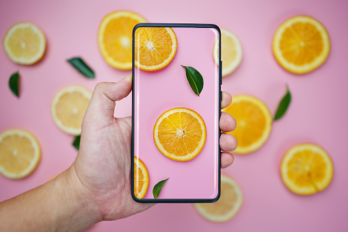 Taking Picture With Infinity Display Smartphone. Orange Lemon Leaves Citrus Pattern on Pink Background Minimal Flat Lay