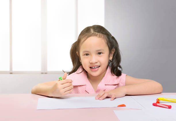 Schoolgirl working in classroom. She is concentrating and writing or drawing in a book. She is wearing a school uniform. Tight crop
