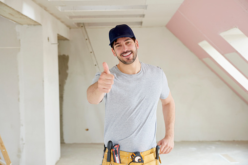 Portrait of young handyman giving thumbs up while standing at construction site.