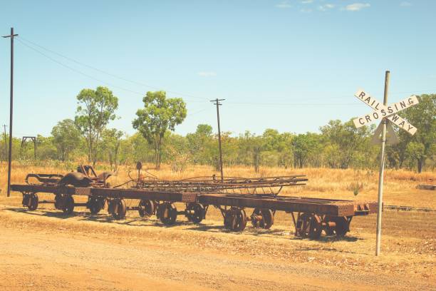 Old rusty train wagon skeletons by railway crossing sign on dirt path in Outback Australia